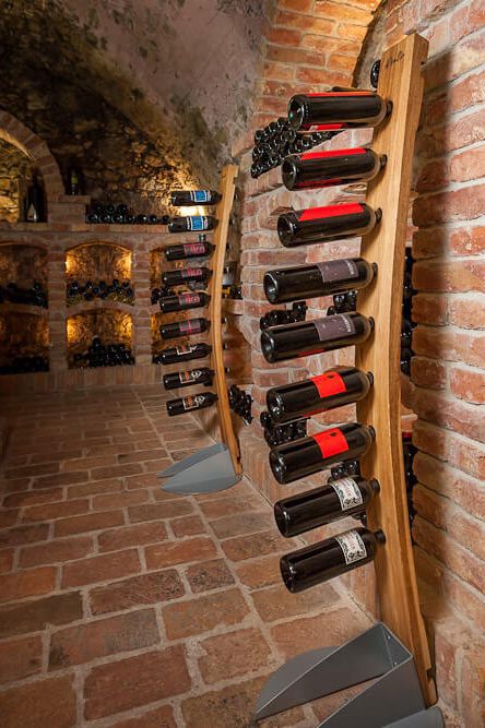 WineSir-Weinhalter in Eiche natur für neun Flaschen mit einem Sockel aus pulverbeschichtetem Stahl steht in einem Weinkeller aus roten Backsteinen. 