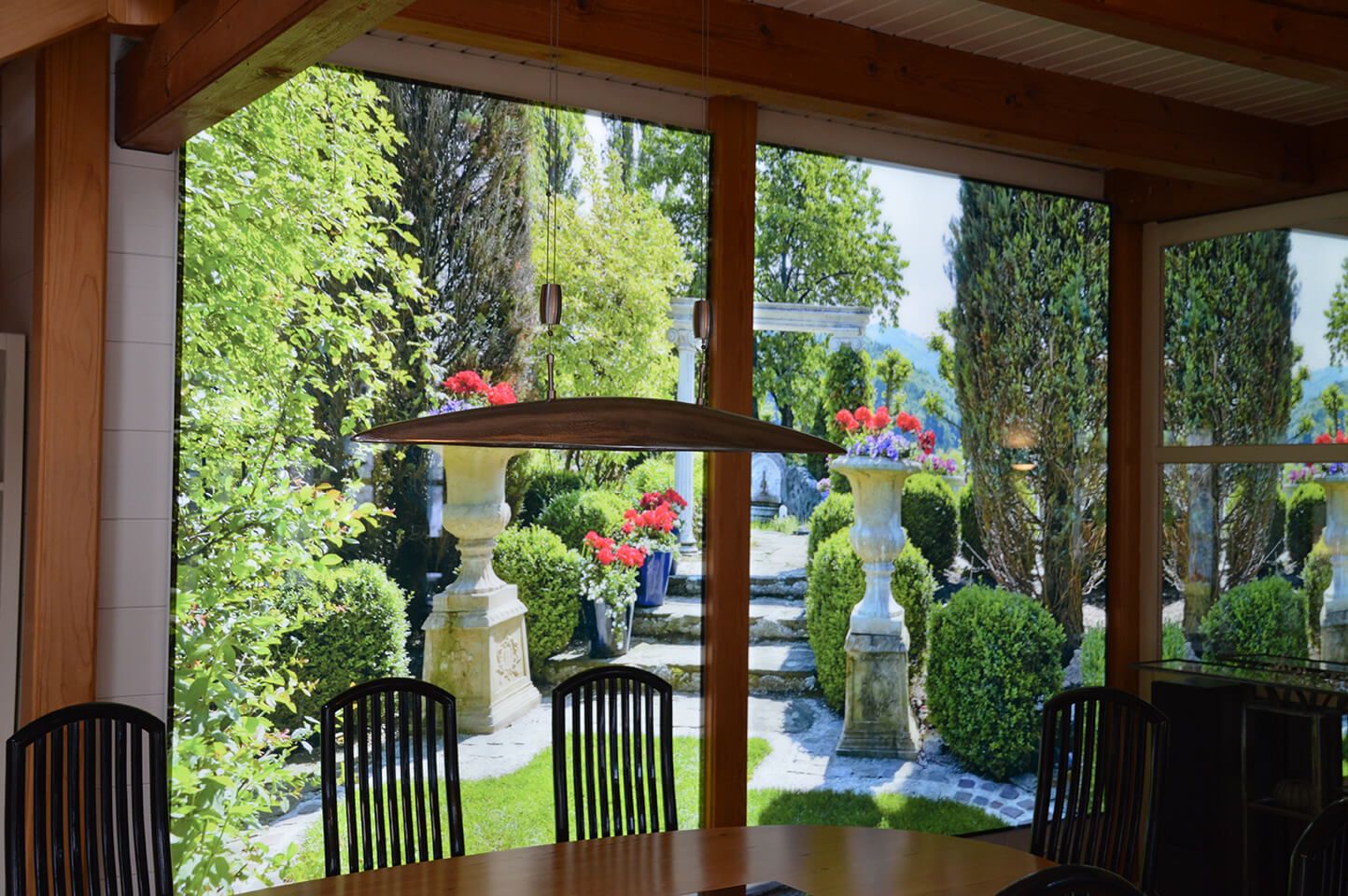 Kundenimpression eines Wandverbaus hinter dem Esstisch mit einem beleuchteten Wandbild mit Motiv südländischer Garten