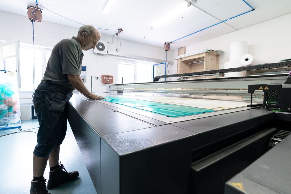 In die Digitaldruckmaschine wird von einem Mitarbeiter soeben Acrylglas eingelegt und für den Druck vorbereitet.